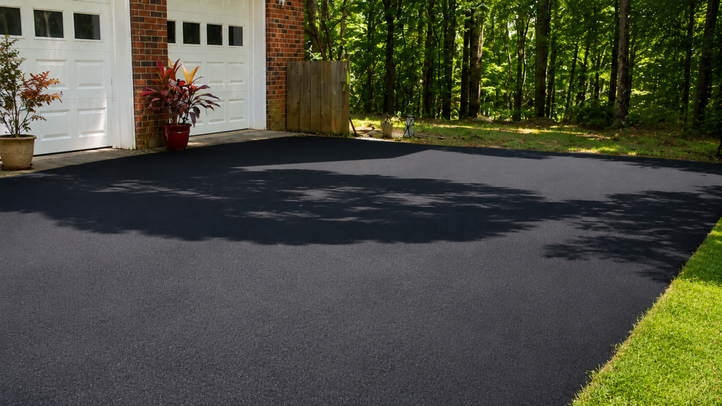 A freshly resurfaced black asphalt driveway in front of a brick garage with trees and matching dappled shadows.
